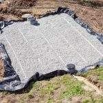 Aerial view of a new sand and gravel filter bed for a septic tank and wastewater disposal shwoing the layout of the filtration pipes, uncut plastic liner and filters and pump