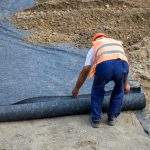 Worker laying geotextile in preparation for new building, used for seperation and reinforcement. Selective focus.
