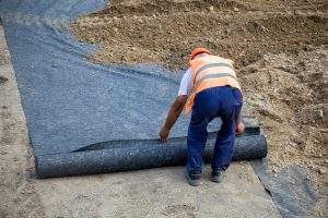 Worker laying geotextile in preparation for new building, used for seperation and reinforcement. Selective focus.