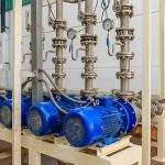 Large industrial water treatment and boiler room. Shiny steel metal pipes and blue pumps and valves.