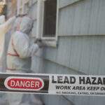 Two house painters in hazmat suits removing lead paint from an old house.