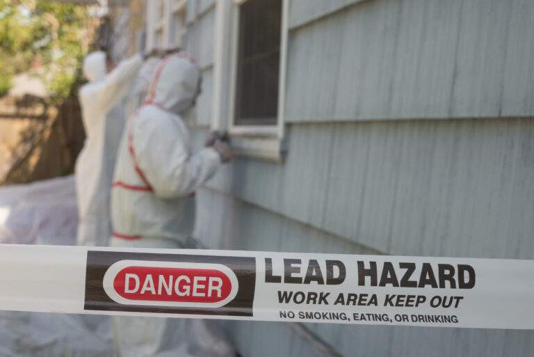 Two house painters in hazmat suits removing lead paint from an old house.