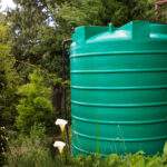 Green water tank in a garden setting with flowers in the foreground