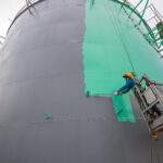 The male worker takes the cable car holding an industrial painting brush used for shell plate tank oil surface surface green color coating.